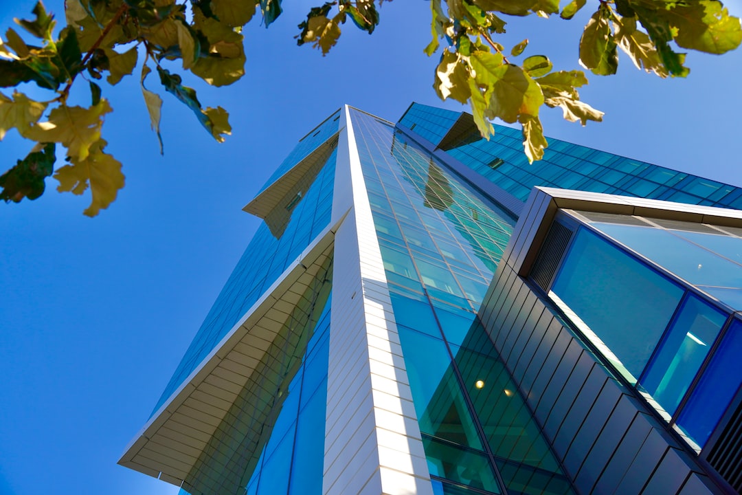 A modern glass and steel building seen from a low angle on Paseo de la Reforma, Mexico City’s luxurious avenue, with green leaves in the foreground and a clear blue sky in the background.