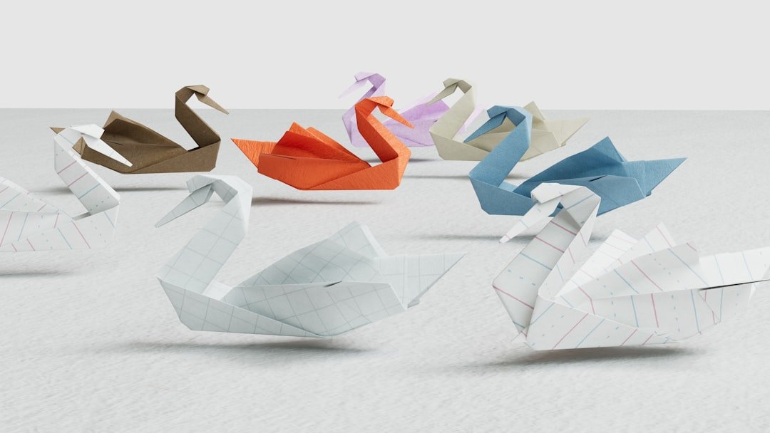 Several origami swans made from different colored and patterned papers are arranged on a light surface, their elegant forms reminiscent of how choosing eyebrow shape can help in perfecting your look against a simple backdrop.