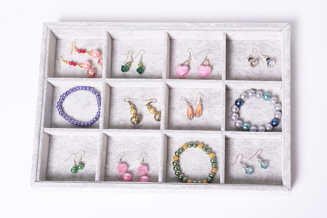 A jewelry organizer with twelve compartments displaying various pairs of prêt-à-porter jewelry earrings and beaded bracelets in different colors and styles.