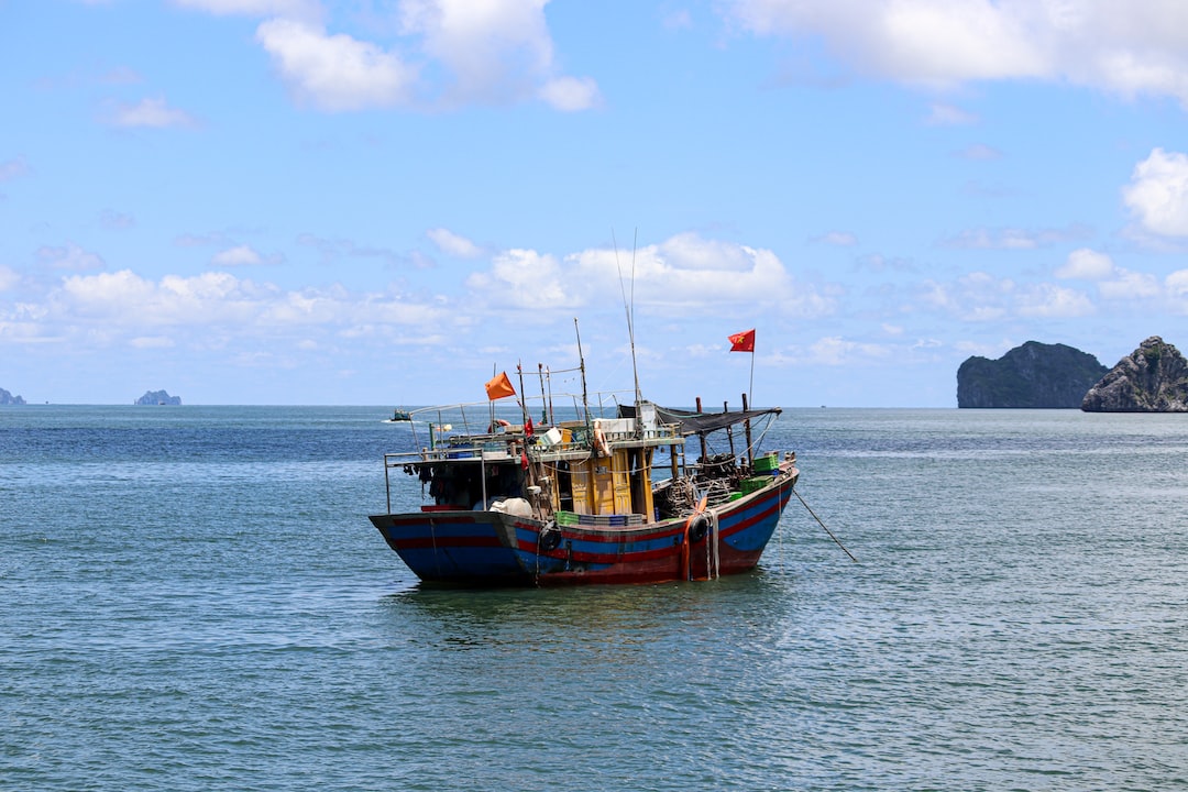 A colorful fishing boat with red flags floats on calm blue water, rocky islands in the background hinting at ultimate seclusion—perfect for those dreaming of private island retreats under a partly cloudy sky.