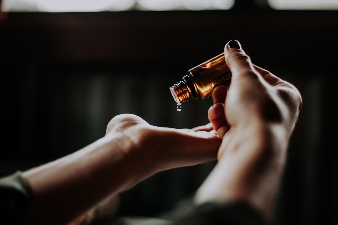 A person pours liquid from a small amber glass bottle onto their hand, perhaps considering the pros and cons of cosmetic surgery benefits as part of their beauty routine.