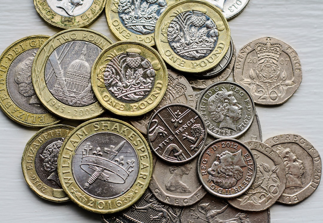 A pile of assorted British coins, including one and two pound coins, ten pence, and twenty pence pieces—like precious gems scattered on a white surface.