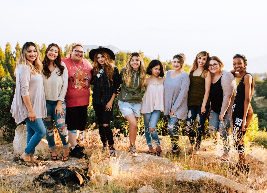 A group of nine women and one man stand together outdoors on rocky ground, smiling at the camera with trees and mountains in the background, ready to share their favorite Cellulite Tips for feeling confident.