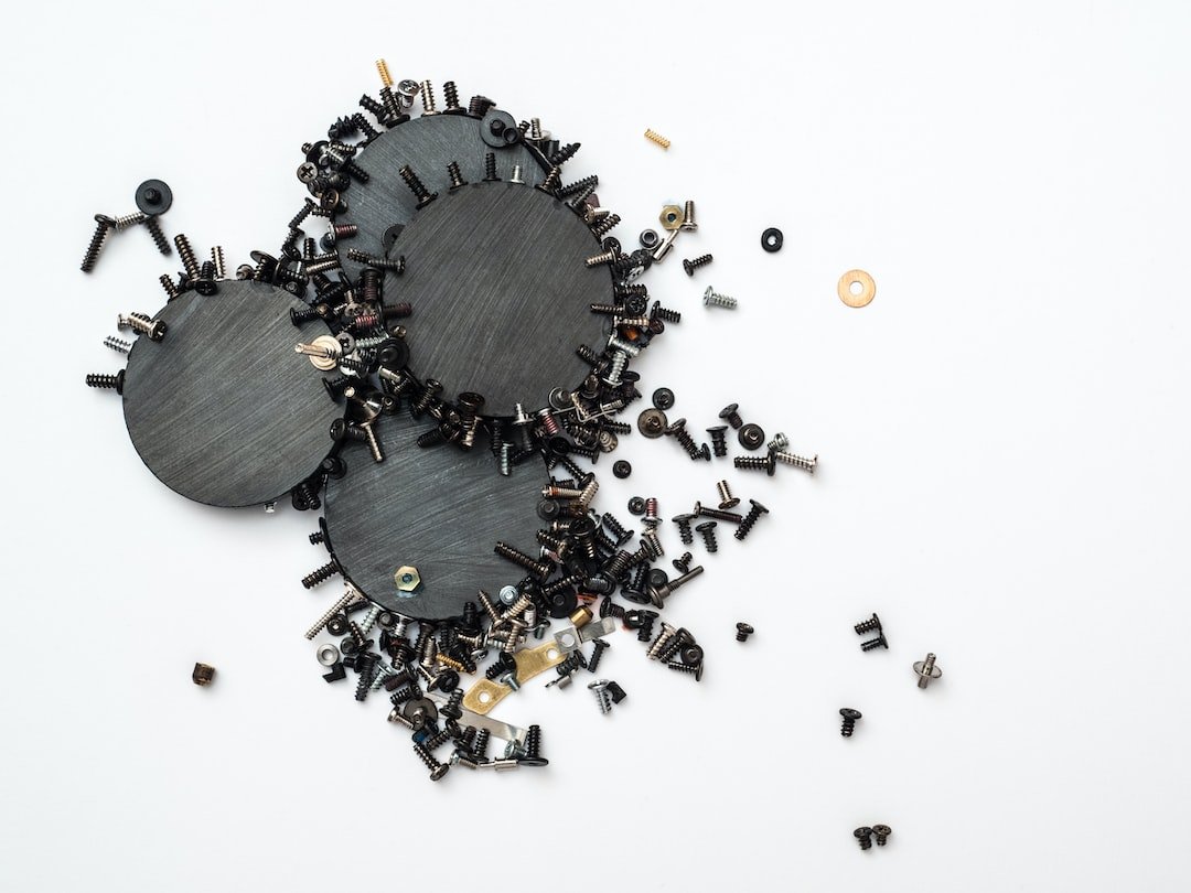 Three black metal discs surrounded by assorted screws, nuts, and washers scattered on a white surface—tools ready to revive delicate pieces during a jewelry repair or to secure precious gems with precision.