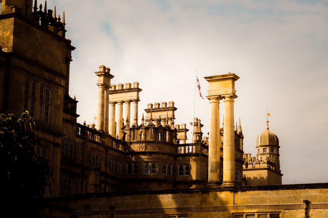 Historic building with numerous tall chimneys and columns, topped with a flag; reminiscent of Copenhagen palaces, part of the structure is bathed in golden sunlight under a partly cloudy sky.