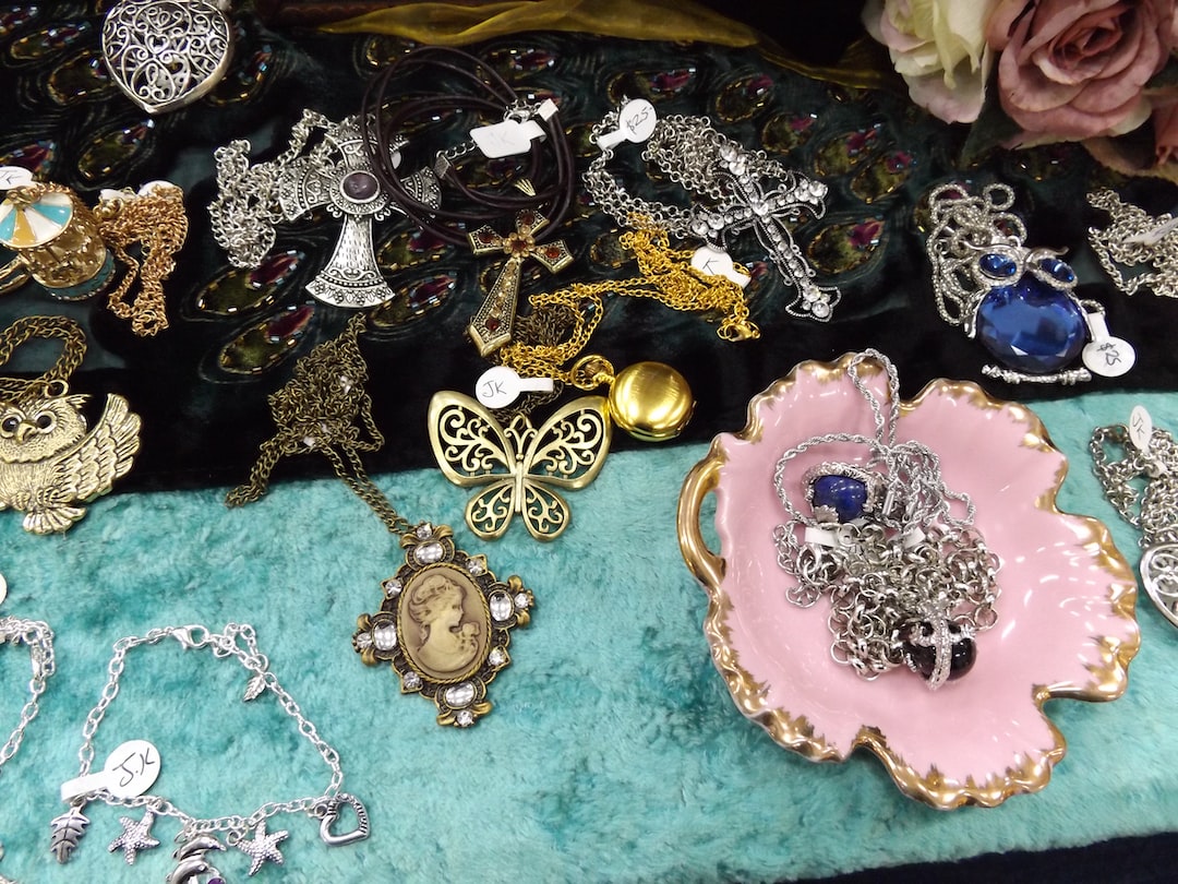A display of assorted jewelry highlighting the latest trends, featuring necklaces, pendants, and bracelets arranged on fabric, with some pieces in a pink dish and artificial flowers in the background for extra shimmer and shine.