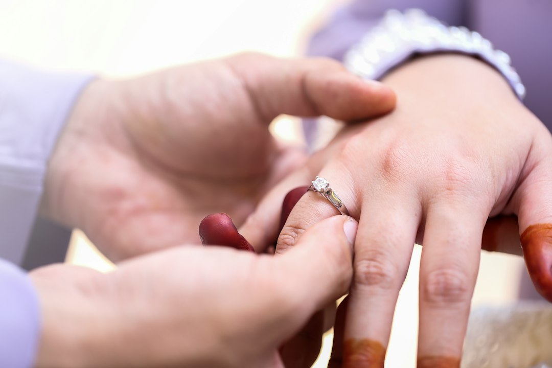A person places a diamond ring on another's finger; both hands have henna stains, beautifully showcasing the importance of jewelry care during special moments.