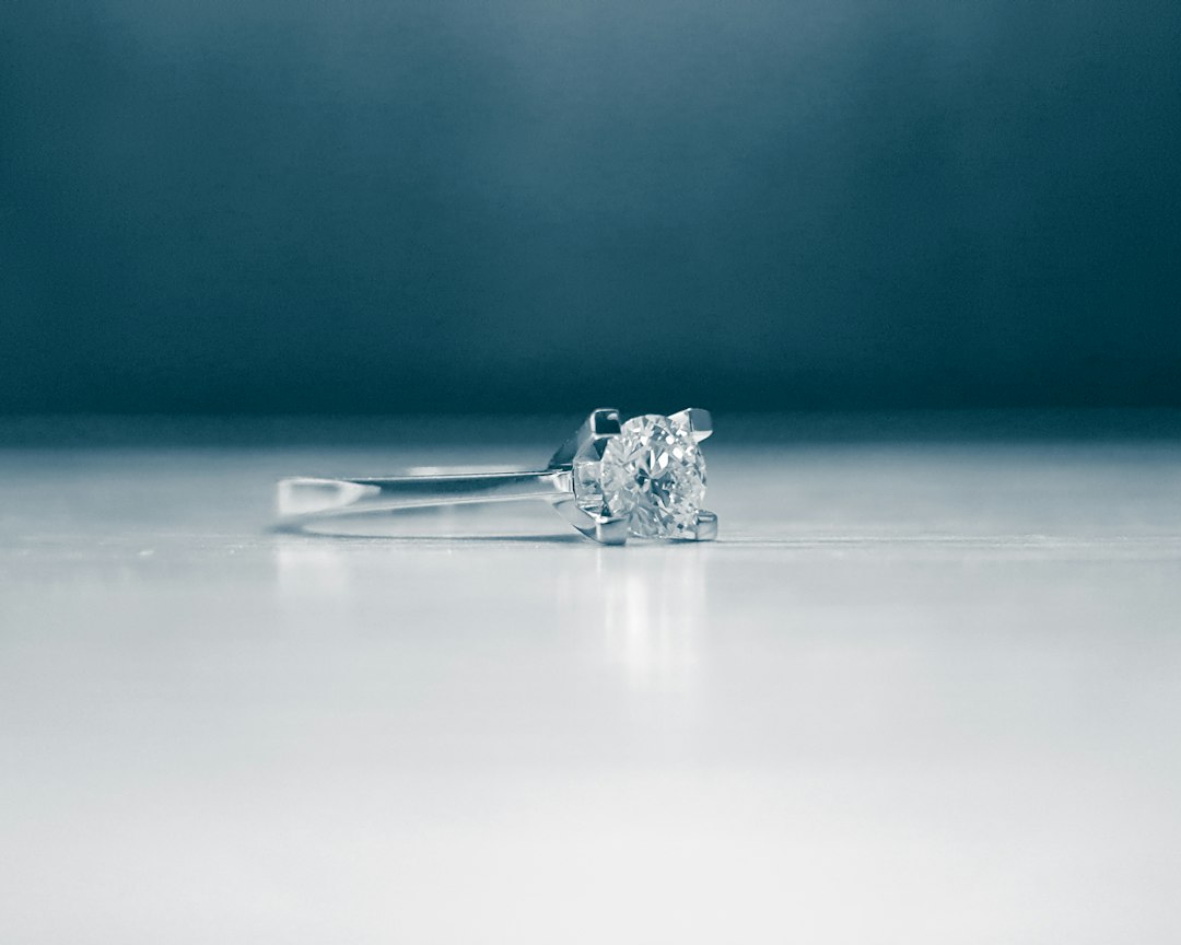 A silver or white gold ring with a single round diamond set in a four-prong setting, displayed on a smooth, light background—a perfect example of timeless elegance.