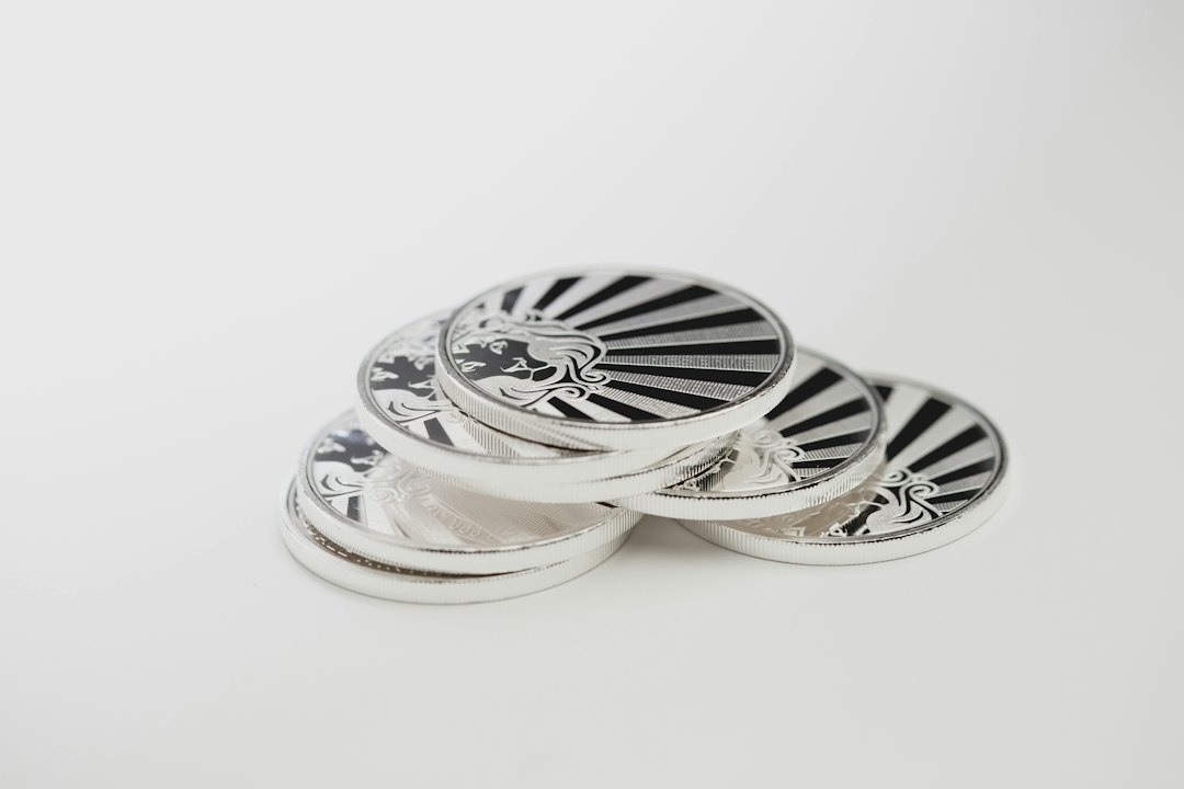 A stack of five silver coins with a sunburst pattern and a stylized profile of a woman engraved on them, placed on a white surface—a striking symbol of investing and timeless value.