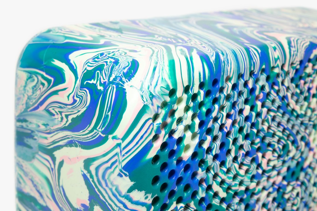 Close-up of a rectangular object with a marbled pattern in blue, green, and white tones, featuring a grid of small, regularly spaced holes—perfect for displaying sustainable jewelry.