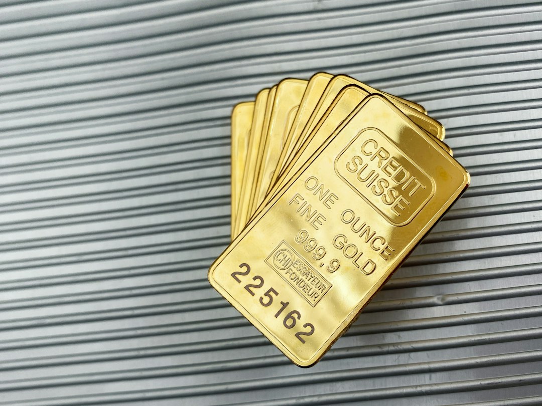 Several stacked one-ounce gold bars labeled "Credit Suisse Fine Gold 999.9" with individual serial numbers, placed on a ribbed metallic surface—a striking symbol of gold investment and portfolio diversification.