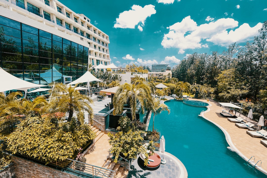 This large hotel with glass windows overlooks an outdoor swimming pool framed by palm trees and lounge chairs, offering the sunny charm of Madrid historic hotels in a luxurious, relaxing setting.