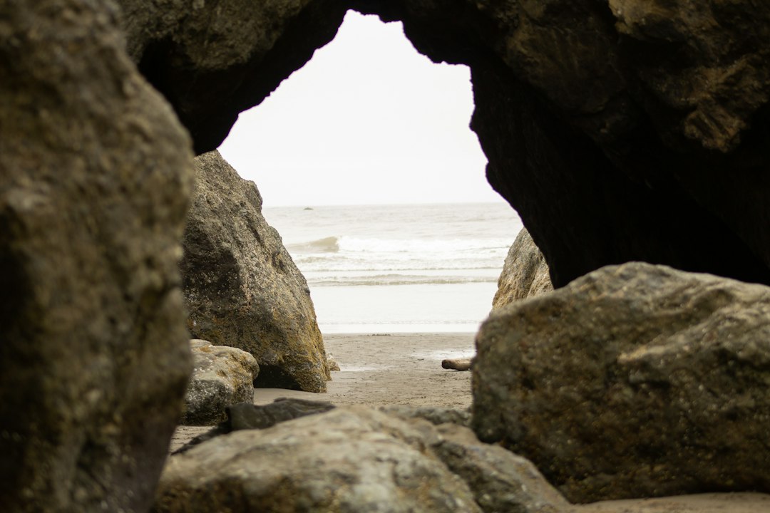 View of the ocean and sandy beach framed by large, rugged rocks forming a natural archway in the foreground—perfect scenery to sparkle in style with elegant Ruby pendants.