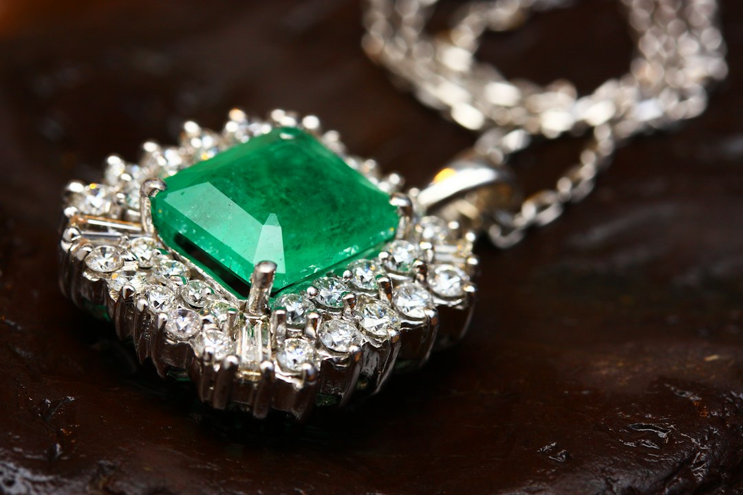 A silver necklace with a square-cut green emerald, surrounded by small round diamonds, captures timeless elegance and sparkling style against a dark background.