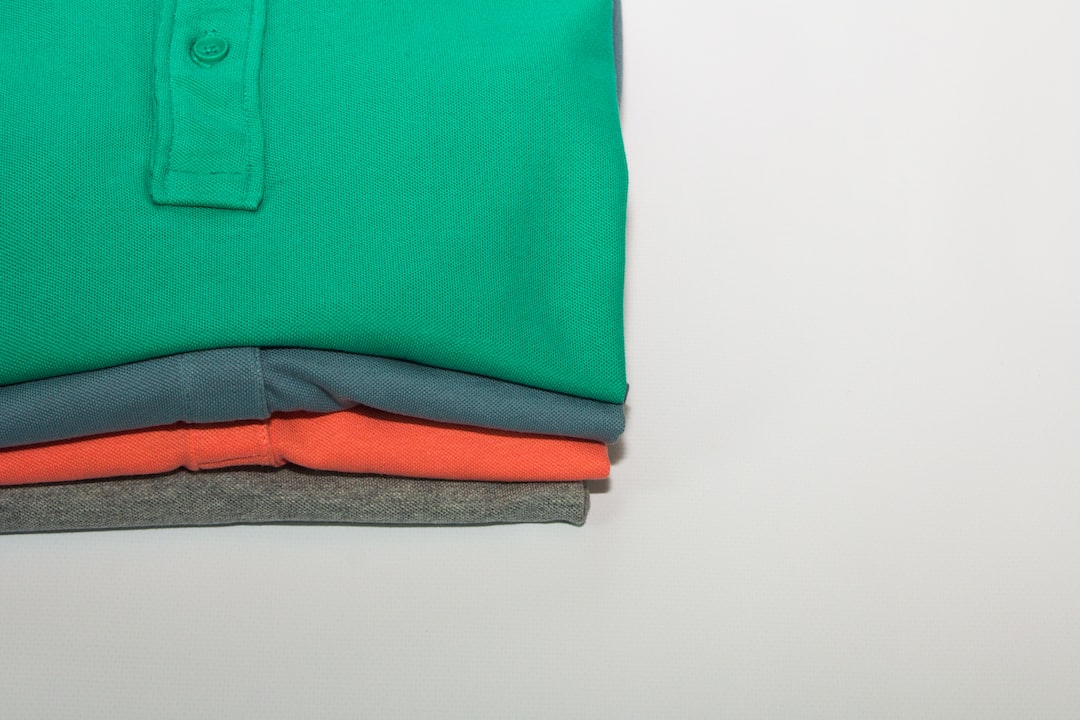 Three folded polo shirts in green, blue, and orange are stacked on a white surface, reflecting Stella McCartney’s signature approach to sustainable luxury fashion.