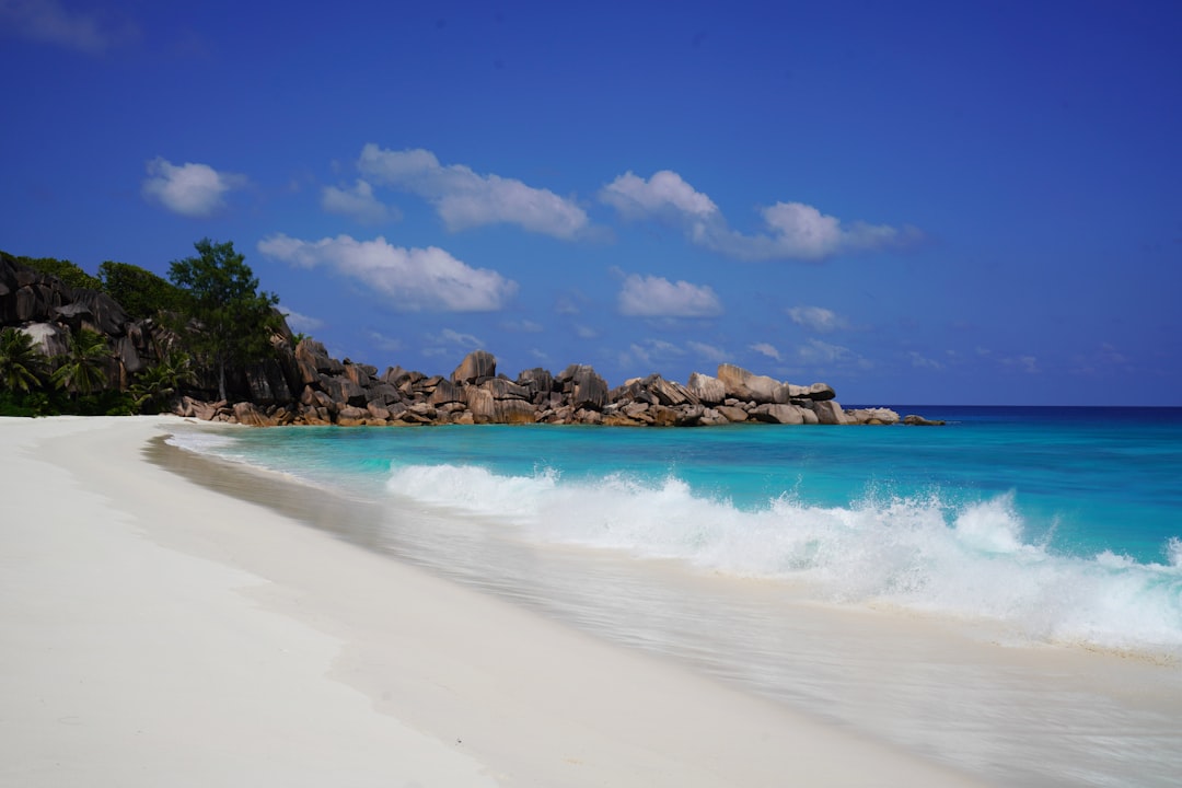 White sandy beach with turquoise water, gentle waves, and rocky outcrops—nature’s summer beauty under a blue sky with scattered clouds.