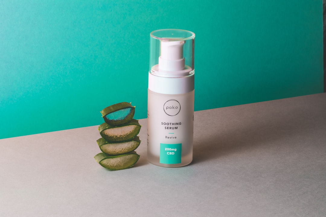 A bottle of Poko Soothing Serum stands next to four stacked slices of aloe vera on a flat surface with a teal and gray background, perfect for achieving glowing skin and enhancing your summer skin care routine.