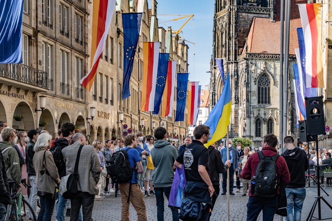 A crowd gathers on a European city street lined with flags, including EU and Ukrainian flags, near historic buildings and a Gothic church—an inviting scene for tailored tours focused on personalized history or memorable historical tours.