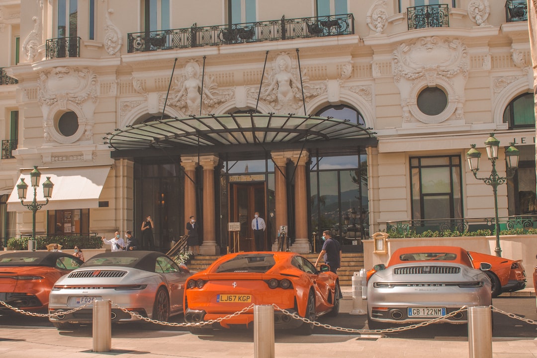 Several luxury sports cars are parked in front of an ornate hotel entrance, evoking the allure of luxury travel and exclusive destinations as guests mingle near the grand doors.