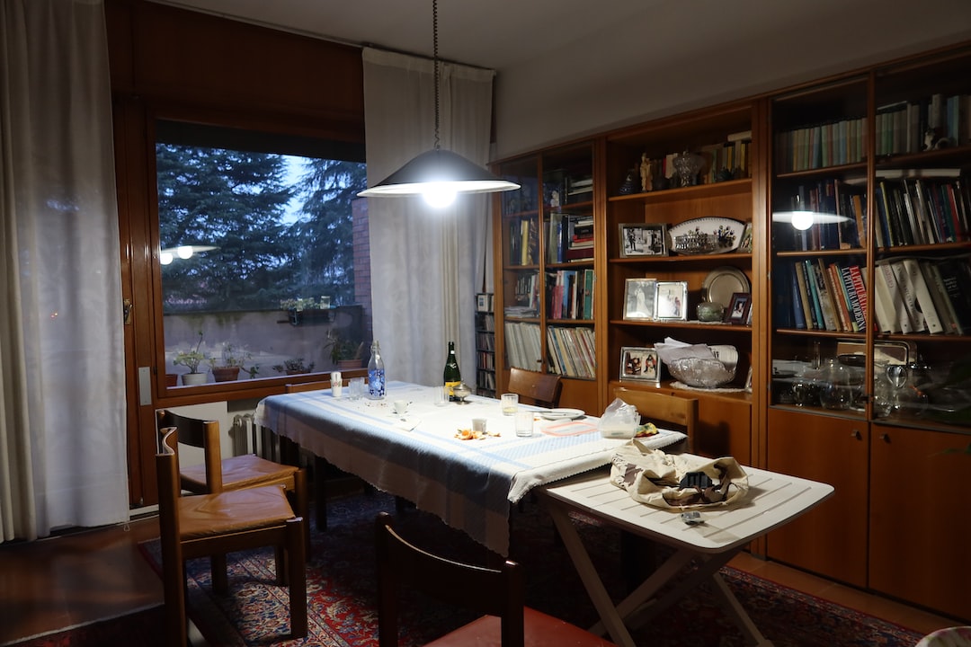 A dining room reminiscent of opulent dining rooms, with a table set for a meal under a hanging light. Bookshelves line the wall, and a large window reveals trees outside, evoking the calm elegance of Michelin-starred restaurants.