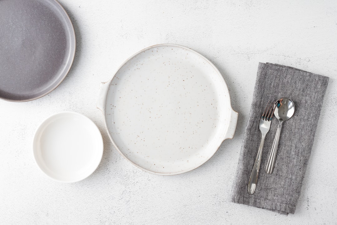 Three empty plates of different sizes and a gray napkin with a spoon, fork, and knife are arranged on a white surface—perfect for elegant home entertaining.
