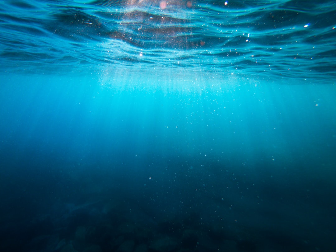 Underwater view showing sunlight rays penetrating the blue water, illuminating particles and evoking the serenity found in underwater restaurants where the art of dining meets mesmerizing aquatic scenery.
