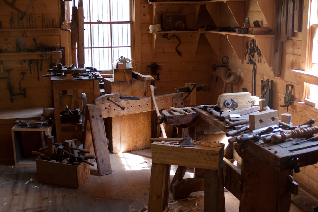 Woodworking shop with benches, hand tools, and wood shavings, lit by sunlight from a window on the left, showcasing handcrafted leather goods alongside finely worked wood.