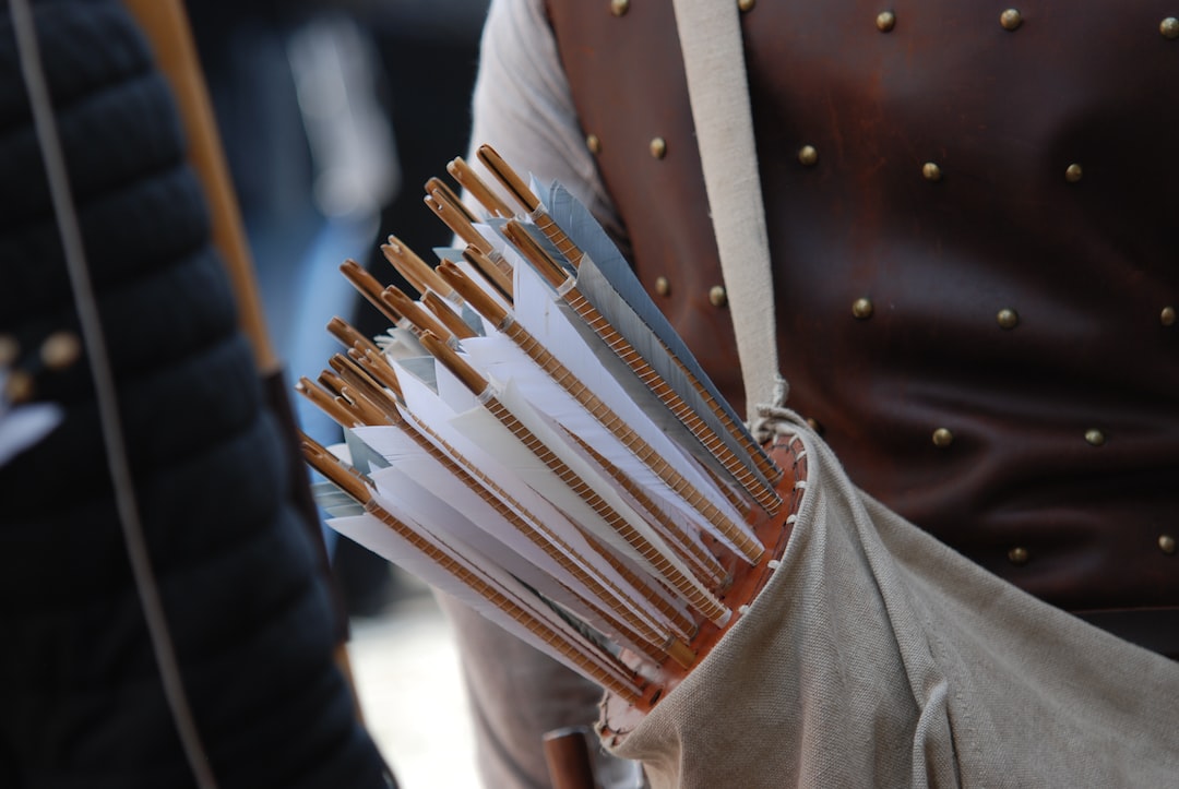 A person wearing a studded leather vest carries a canvas quiver filled with wooden arrows with white fletching, ready for archery.