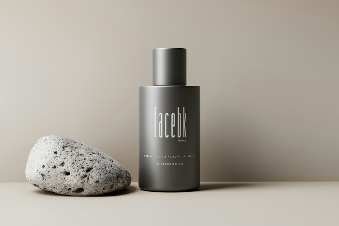 A gray bottle labeled "facebk" stands upright next to a textured stone on a neutral background, evoking luxury branding and creating a timeless image with its refined, minimalist aesthetic.