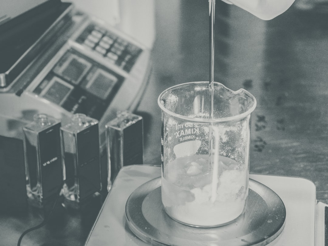 Clear liquid is poured into a beaker of white substance on an electronic scale, capturing the precision of luxury perfume making in a Paris laboratory setting.