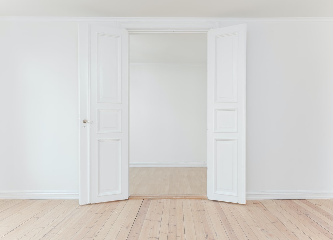 A pair of white double doors open into an empty, light-filled room with white walls and light wooden floors, evoking the serene elegance found in luxury train suites.