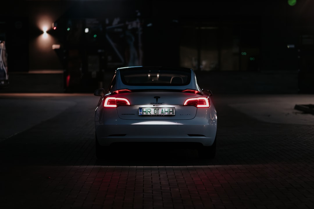 A white Tesla car with illuminated tail lights, symbolizing the elegance of high-end jewelry, is parked at night on a paved area, seen from behind.