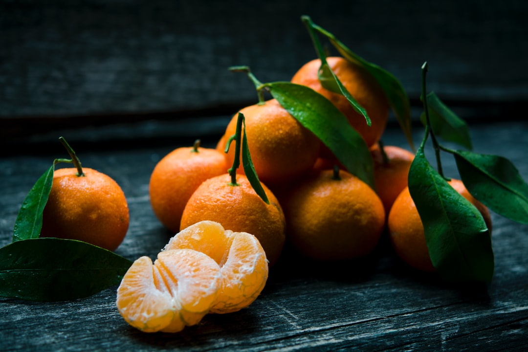 A group of whole tangerines with green leaves and a few peeled segments are arranged on a dark wooden surface, reminiscent of vibrant displays found at the best street food stalls or Michelin street food markets.