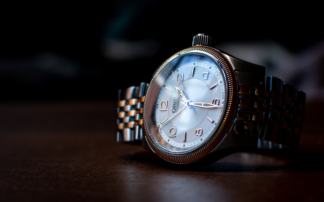 A close-up of a silver wristwatch with a metal band, evoking modern luxury, rests on a wooden surface and shows the time at 2:16.