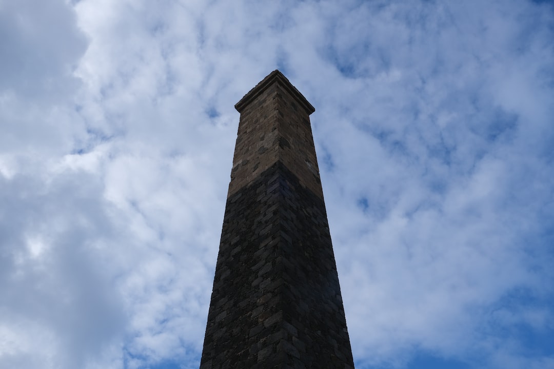 A tall, stone obelisk rises vertically against a background of blue sky with scattered clouds, its enduring presence echoing the timeless craftsmanship found in luxury timepieces.