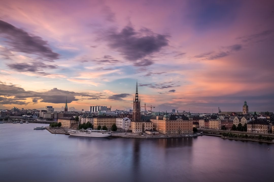 Stockholm’s skyline features historic buildings and a tall church spire at sunset, with calm water in the foreground and colorful clouds painting the sky, reflecting an elegant blend of city lifestyle and timeless beauty.