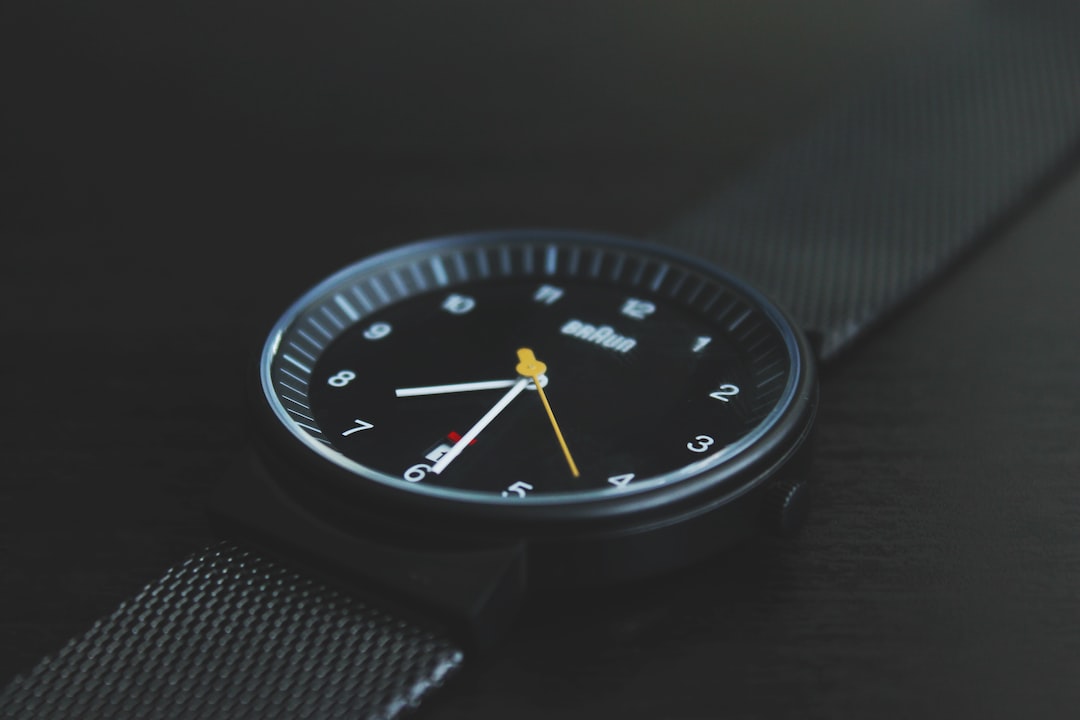 A black Braun wristwatch with a mesh band is shown close-up, its modern design echoing the evolution seen in the Glashütte Original Senator Collection, displaying the time as 10:08:36 against a dark background.