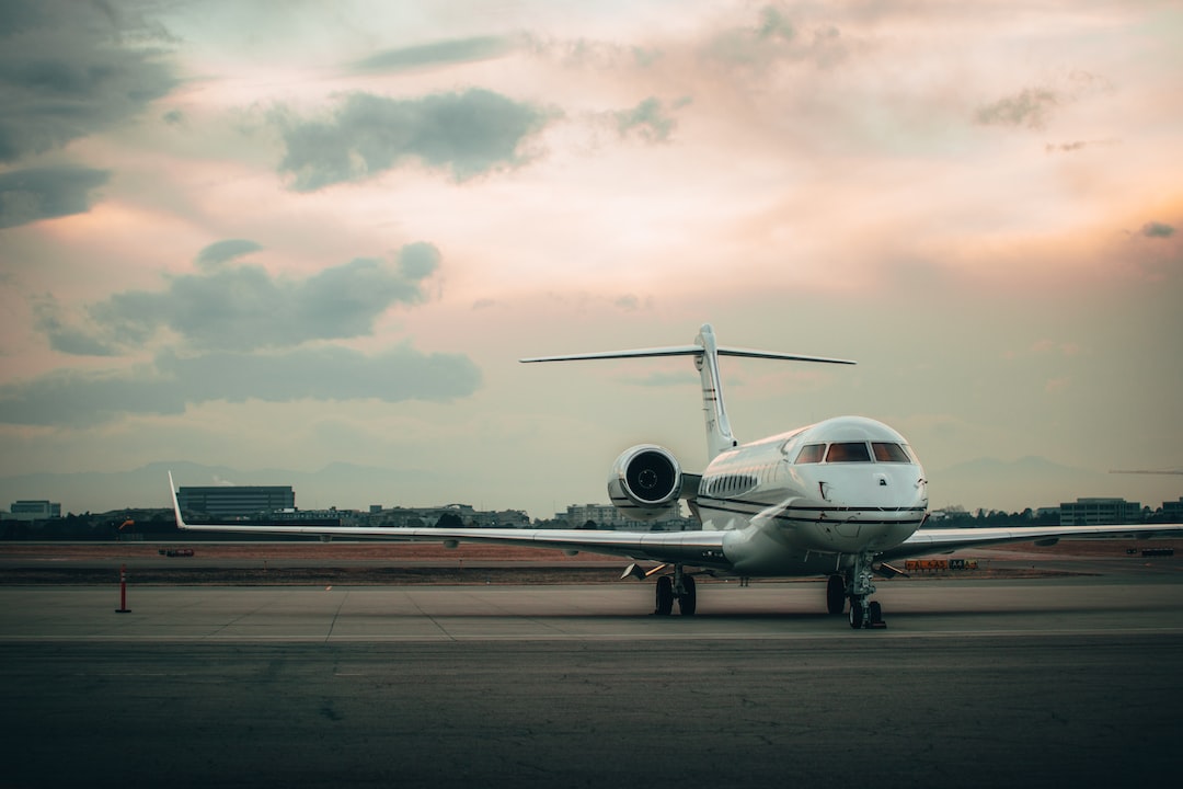 A private jet, symbolizing the evolution of air travel, is parked on an airport runway at sunset, with buildings and mountains visible in the background beneath a cloudy sky.
