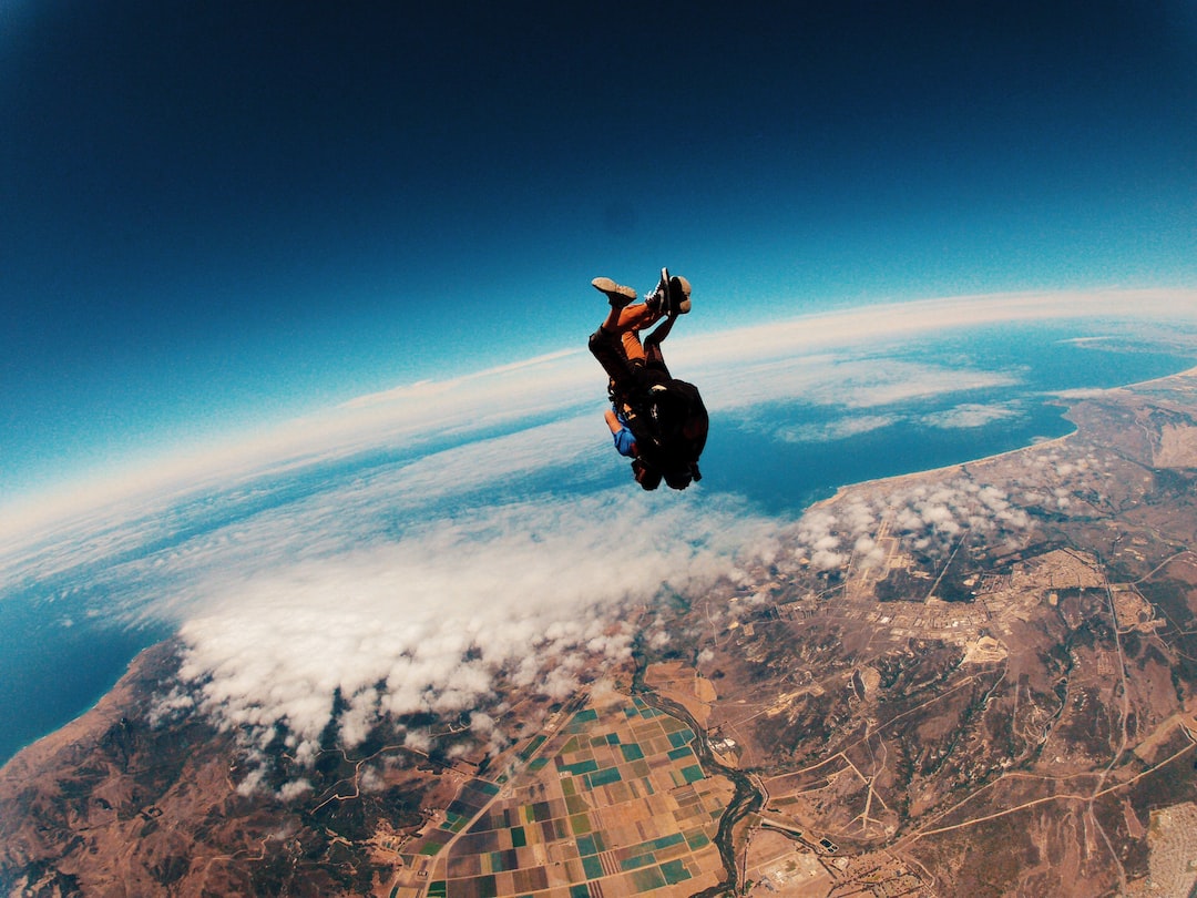Two people tandem skydiving above land and clouds, with a view of fields, coastline, and the ocean below—a thrilling weightlessness experience reminiscent of zero gravity flights.