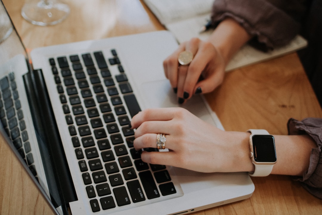 A person wearing a smartwatch and rings types on a laptop with a notebook open nearby on a wooden desk, embodying the seamless connectivity found in the future of smart homes.