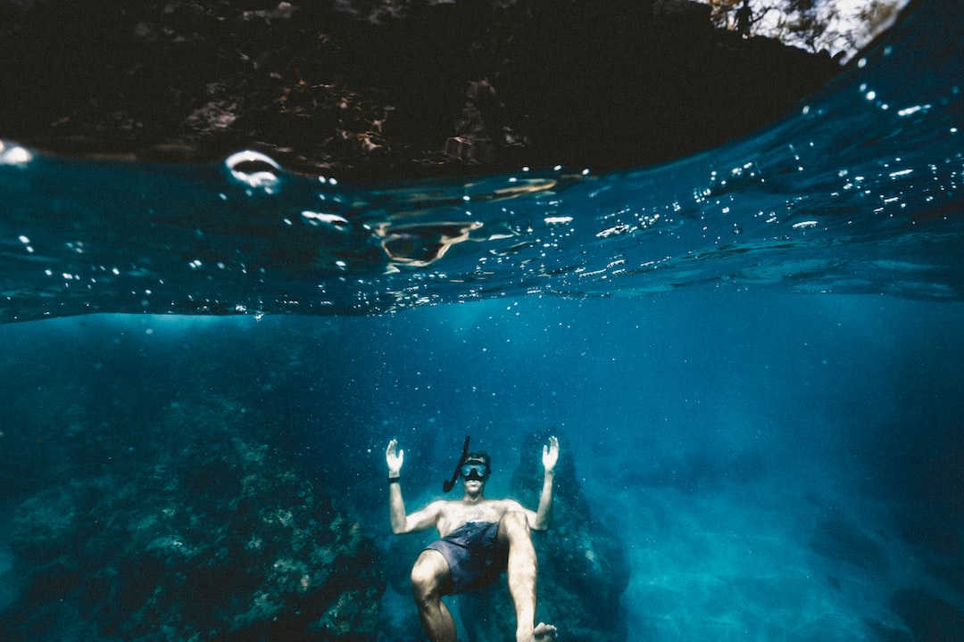 A person wearing snorkeling gear floats underwater near the surface with arms raised, seen from a split-level view—a scene reminiscent of the future of underwater resorts and luxury underwater hotels.