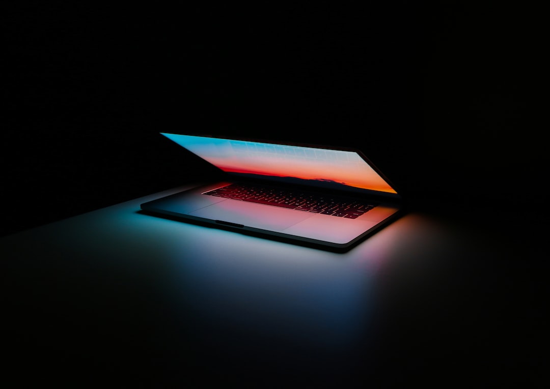 A partially closed laptop emits colorful light on a dark surface, its screen displaying a gradient of sunset colors, highlighting the sleek design inspired by technology and luxury car manufacturing.