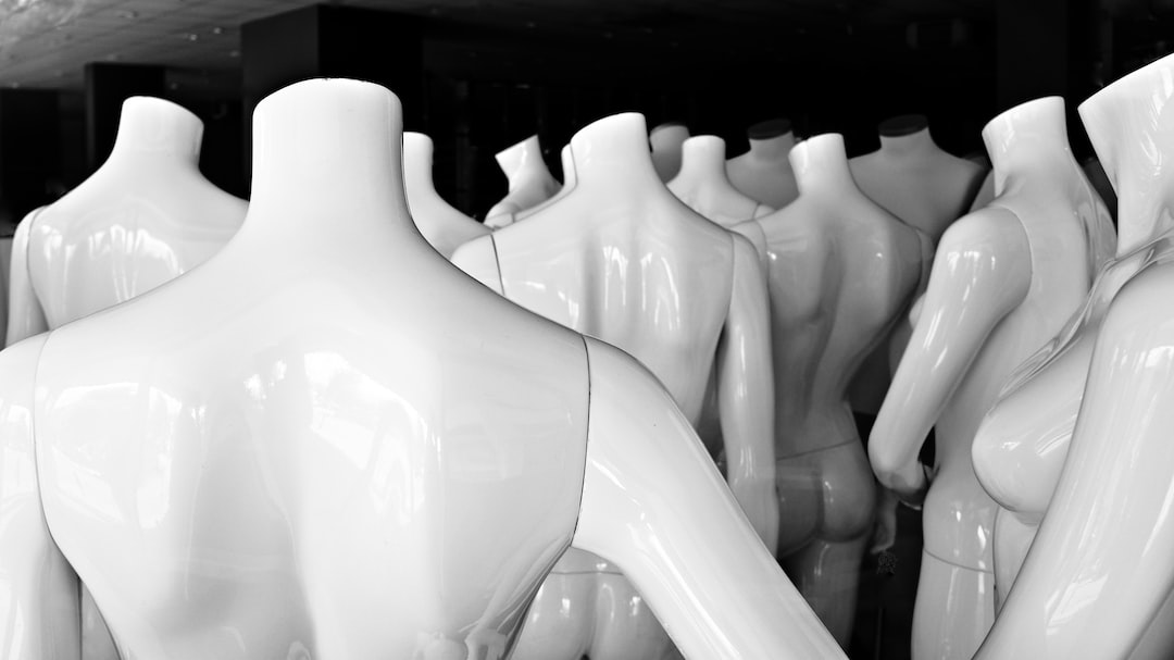 A group of glossy, headless white mannequins are closely arranged in a display, viewed mostly from the back, evoking innovative aesthetics reminiscent of high fashion installations.