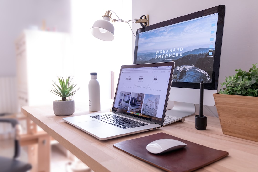 A tidy workspace with a laptop, desktop monitor, keyboard, mouse, water bottle, potted plant, and desk lamp on a wooden desk. The monitor displays "WORKHARD ANYWHERE," blending productivity with the style of cutting-edge home theaters.