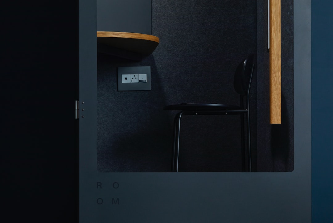 A black chair and a wooden desk inside a small, dark, modern booth with a power outlet on the wall—ideal for planning your next luxury chartering adventure or working remotely aboard private superyachts.