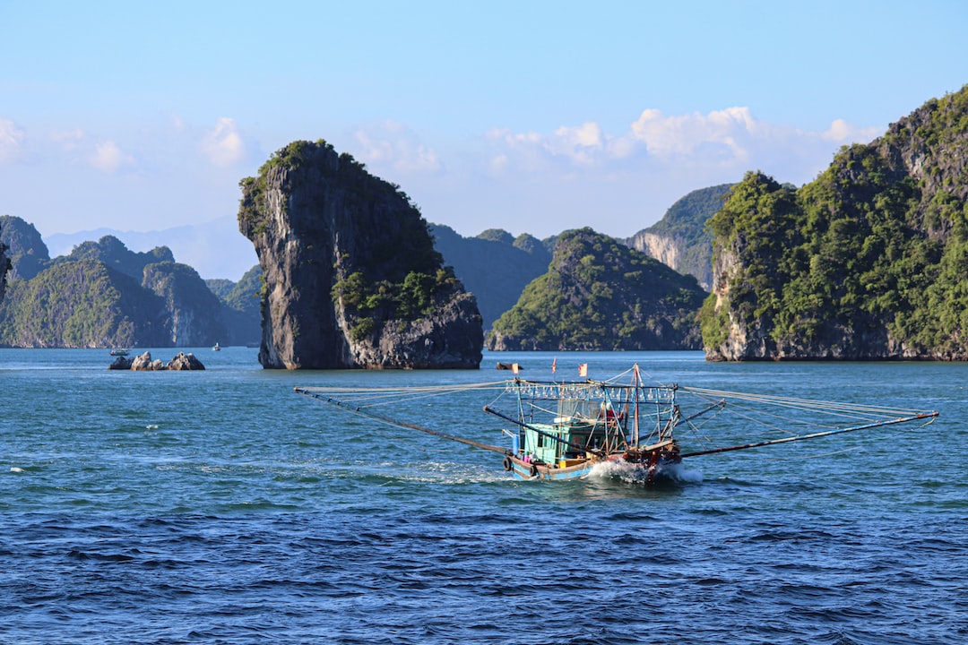 A fishing boat with extended outriggers moves through blue water, passing rocky, tree-covered hills—the perfect scene for an island getaway under a clear sky.