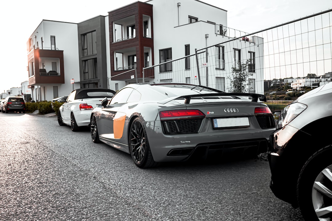 A gray Audi R8 sports car is parked on a street in front of modern residential buildings, reflecting the psychology of luxury and the allure of luxury consumption among urban dwellers, with other cars parked nearby.