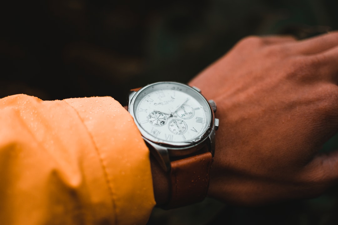 A close-up of a wrist wearing a brown leather strap vintage luxury watch with a white face, Roman numerals, and multiple dials. The person is wearing a yellow jacket—a timeless piece for modern collecting.