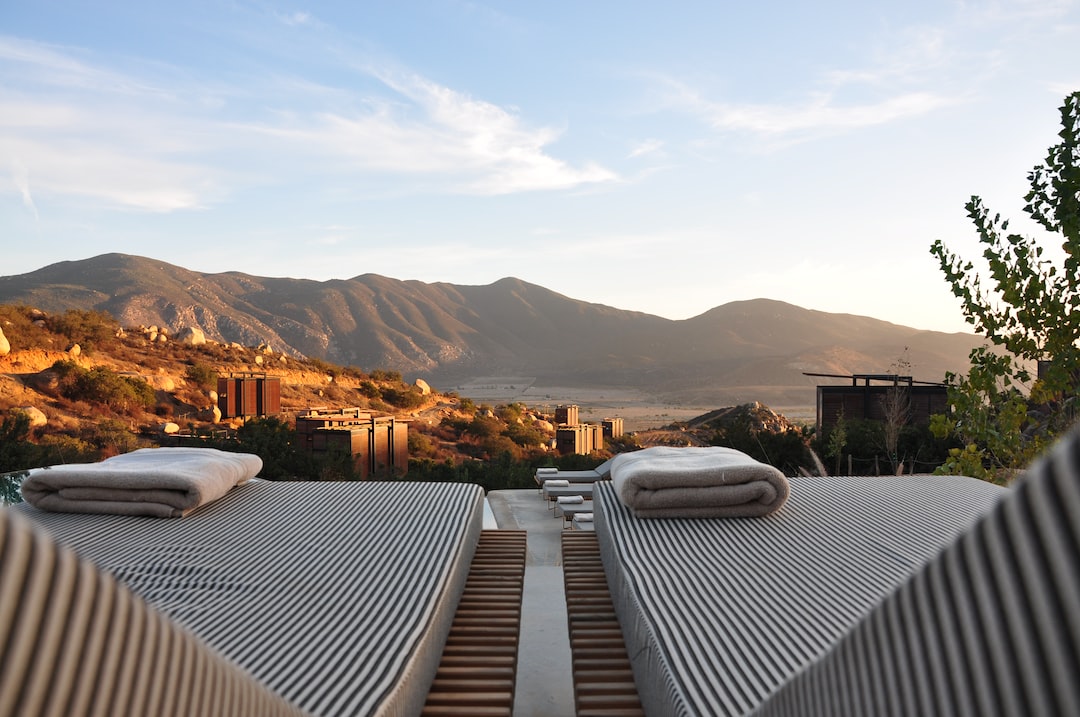 Two lounge chairs with rolled towels face a scenic view of distant mountains and a sunset valley, overlooking a luxury resort complex offering personalized luxury services below.