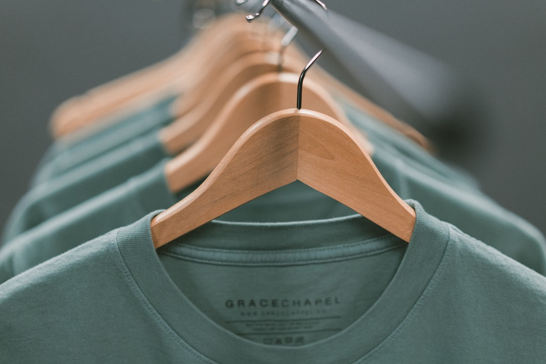Several green t-shirts, part of our personalized luxury apparel collection, are neatly arranged on wooden hangers along a clothing rack.